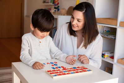 Mother assisting son in puzzle sitting at home