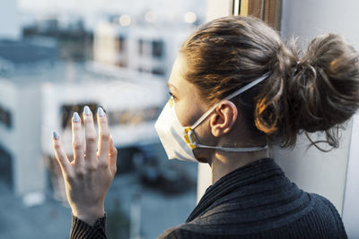 Rear view of woman wearing mask by window