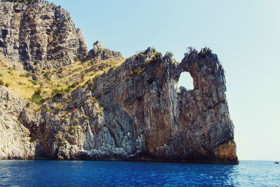 Rock formation in sea against clear sky