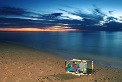 Deck chair at beach against sky during dusk