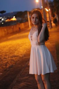 Portrait of beautiful woman in dress standing on street at night