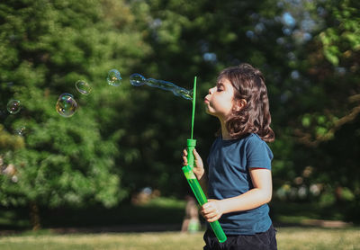 Portrait of a beautiful caucasian girl blows soap bubbles standing in the park