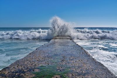 Sea waves splashing on shore against clear sky