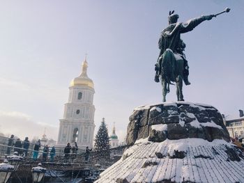 People looking at snow covered statue against church during christmas