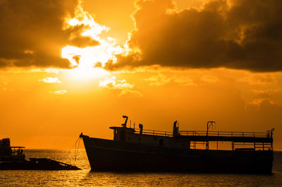 Silhouette boat moored in caribbean sea against cloudy sky during sunrise