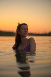 Portrait of young woman swimming in lake during sunset