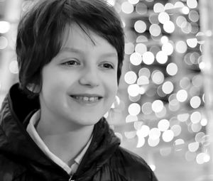 Close-up of thoughtful boy smiling against illuminated lights