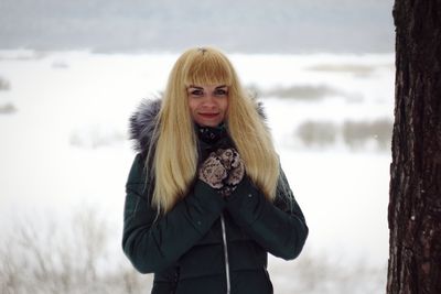 Portrait of young woman standing in snow against sky