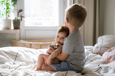 Cute brother sitting with sister on bed