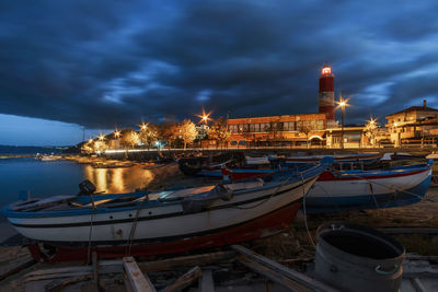 Boats moored on sea against illuminated buildings in city at night