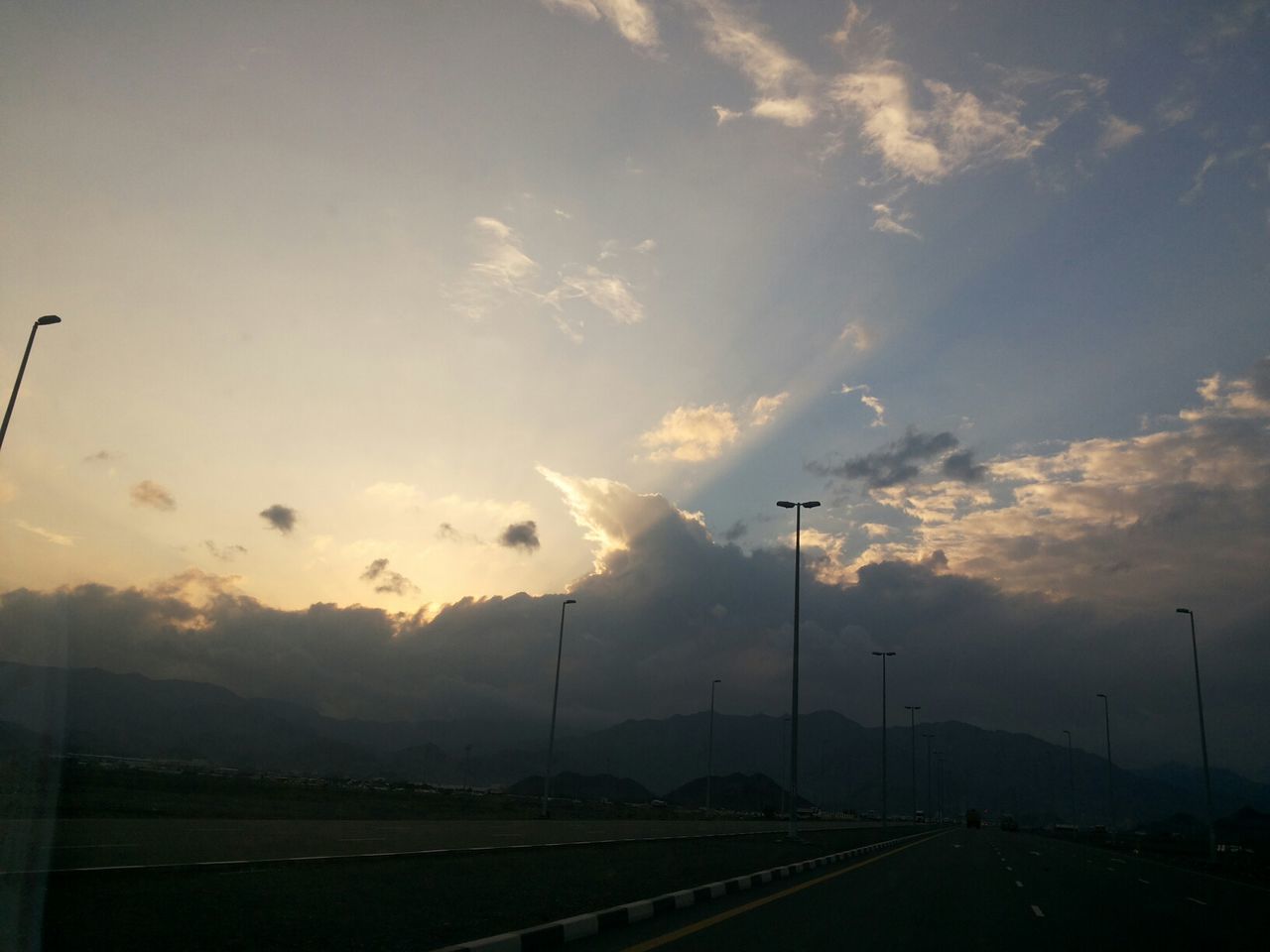 sunset, sky, road, street light, transportation, the way forward, scenics, tranquility, cloud - sky, landscape, tranquil scene, beauty in nature, nature, electricity pylon, diminishing perspective, cloud, road marking, silhouette, cloudy, outdoors