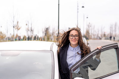 Portrait of young woman standing by car on road