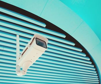 Low angle view of security camera hanging from turquoise ceiling
