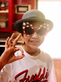 Portrait of smiling teenage girl gesturing ok sign while wearing sunglasses at home