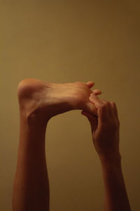 Cropped hand of woman holding leg against wall
