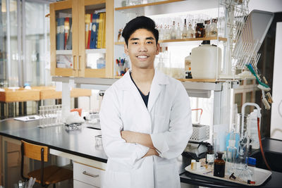 Portrait of confident young male university student standing with arms crossed at chemistry laboratory