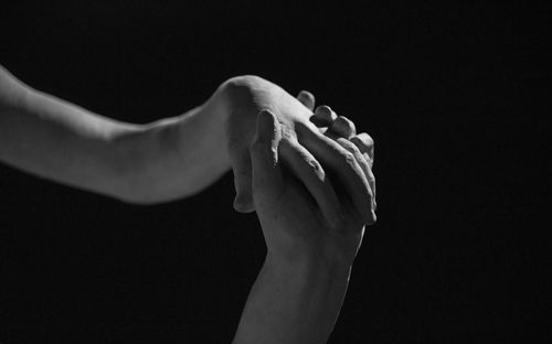 Close-up of hand holding leaf over black background