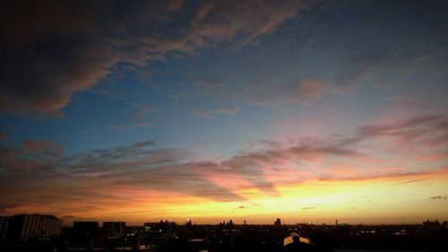 Silhouette city against dramatic sky during sunset