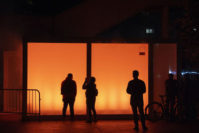 Silhouette people standing by illuminated bicycle during sunset