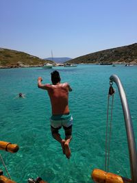 Rear view of shirtless in sea against clear sky