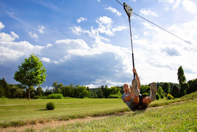 Full length of man screaming while zip lining against sky on field