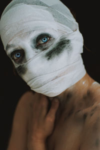 Portrait of young woman with bandage covering face against black background