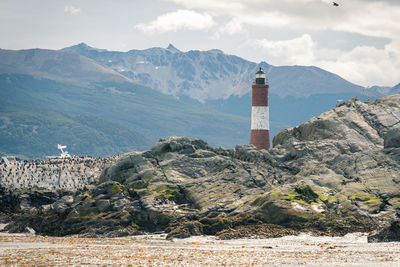 Lighthouse amidst buildings and mountains against sky