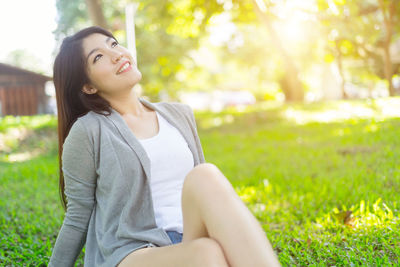 Happy young woman sitting on grassy field at park