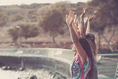 Female friends with arms raised standing at bridge