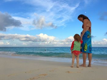 Full length of mother with daughter standing at beach against sky