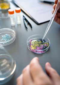 Female chemist adding drop of liquid from from pipette over petri dish with mix of glitters in lab