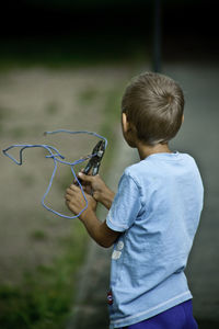 Rear view of boy clipping blue cable with plier