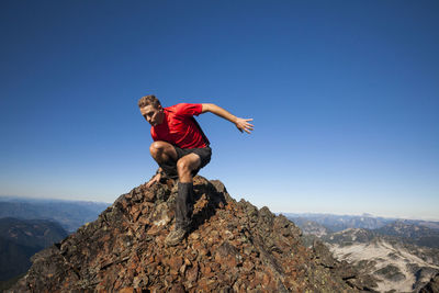 Man moving down from rocky mountain against clear blue sky during sunny day