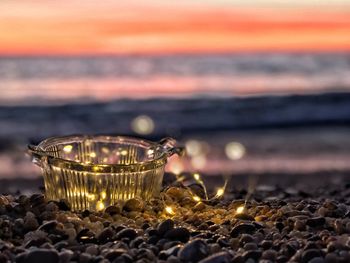 Close-up of illuminated lamp on beach at sunset