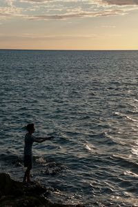 Man standing in sea against sky during sunset