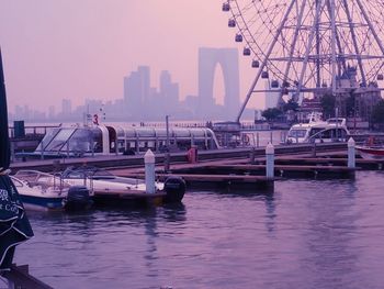 Boats moored in river against cityscape during sunset