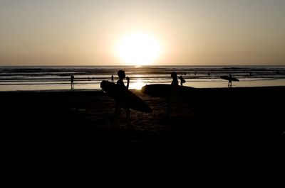 Silhouette people on beach against sky during sunset