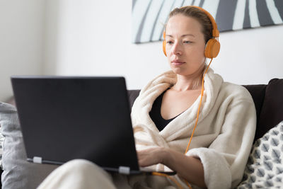 Mid adult woman listening music sitting on sofa at home