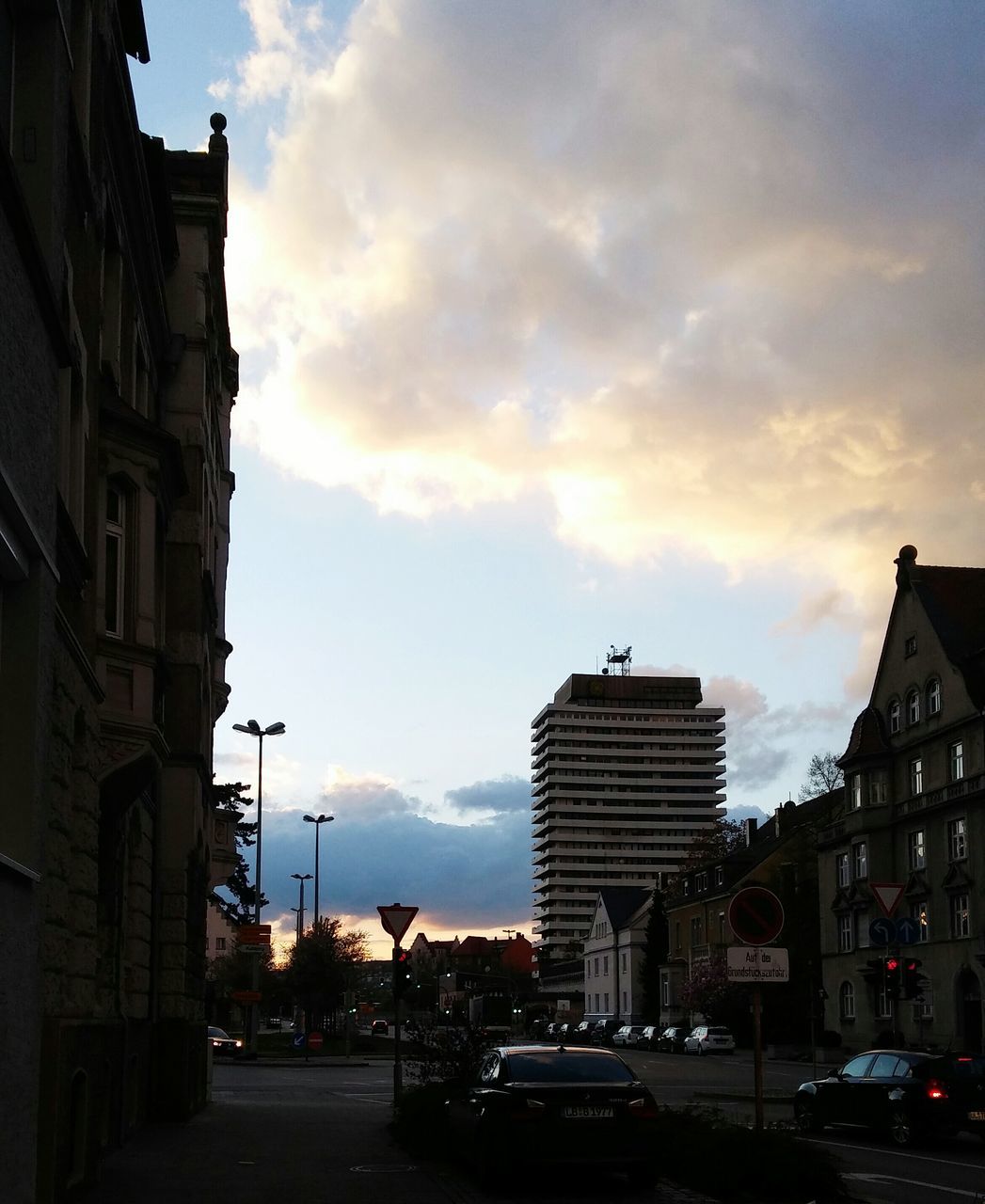 building exterior, car, architecture, transportation, built structure, land vehicle, street, sky, city, mode of transport, road, sunset, cloud - sky, street light, building, city street, cloud, city life, the way forward, residential building