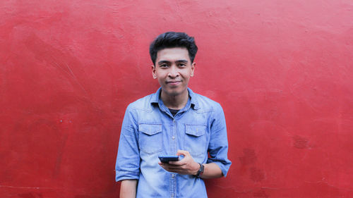 Portrait of smiling young man standing against red wall