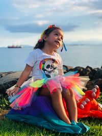 Girl looking away while sitting on grass against sea and sky