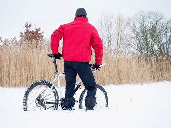 Rear view of man with bicycle on snow field