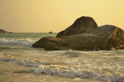 Rocks in sea against clear sky during sunset