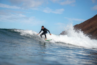 Full length portrait of man surfing in sea against sky