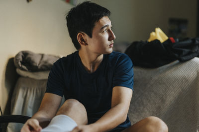 Teenage male athlete looking away while day dreaming at home