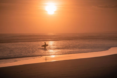 Silhouette person on beach against sky during sunset