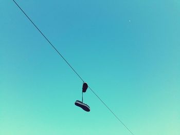 Low angle view of abandoned shoes hanging from cable against clear sky