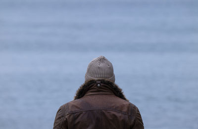 Rear view of adult man in leather jacket against sea