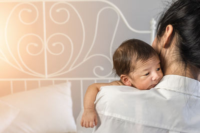 Close-up of woman holding newborn son on bed at home