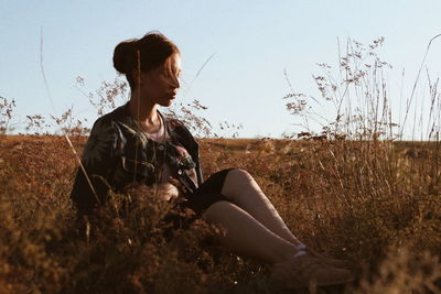 Side view of man sitting on field against sky